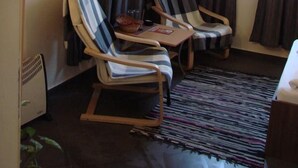 Quarto com duas poltronas listradas, uma mesa pequena com uma tigela e um controle remoto, e uma televisão fixada na parede.