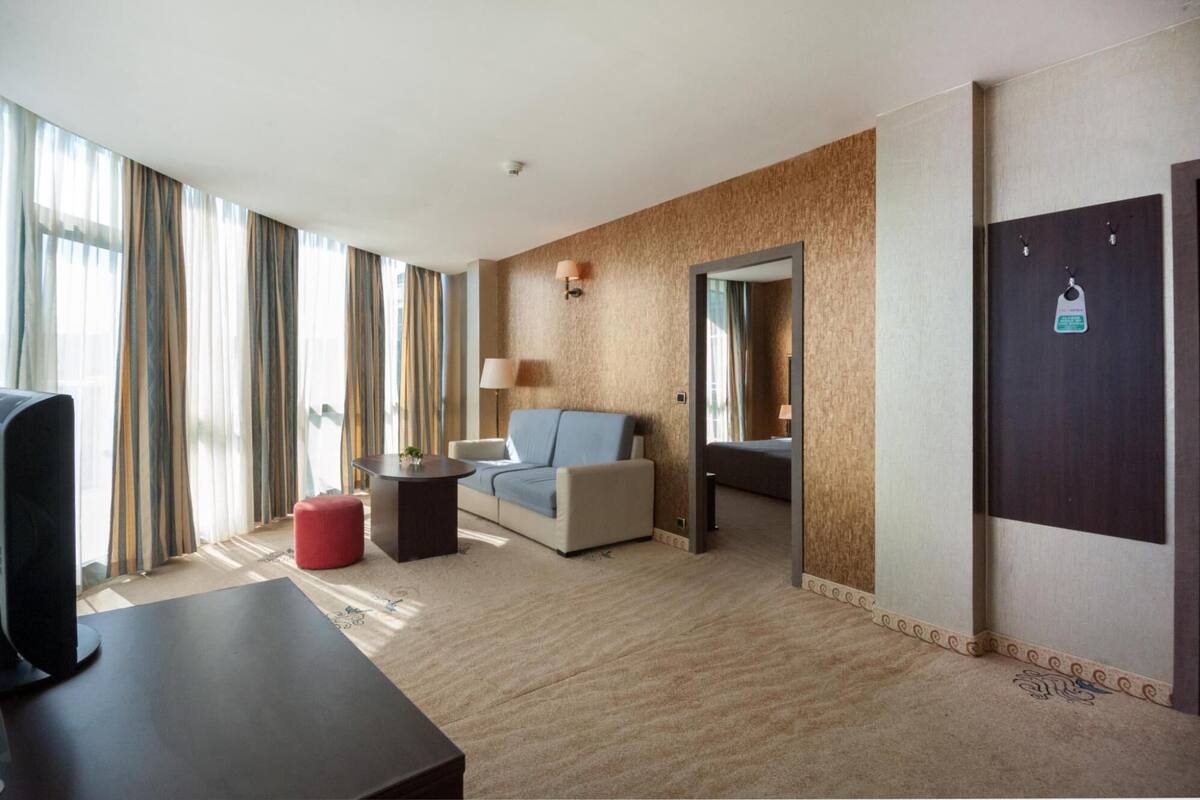 A hotel room with a bed, a sofa, a TV, a desk, and a mirror.