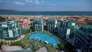 Un resort con piscina central, varias construcciones y vista al mar.