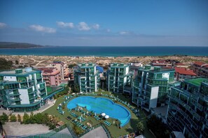 Un resort con piscina central, varias construcciones y vista al mar.