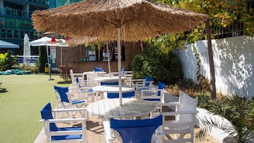 Outdoor seating with white tables and blue chairs, a thatched umbrella, and a building in the background.