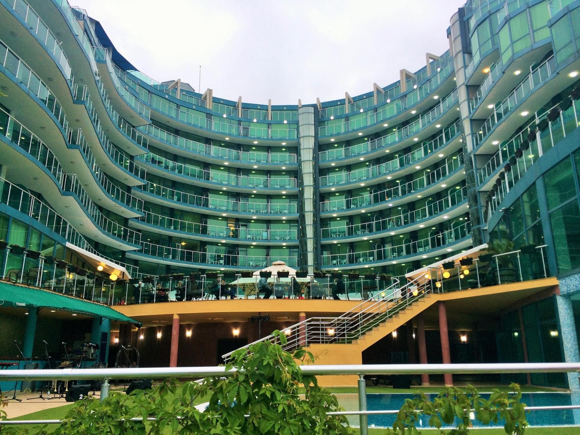 A multi-level hotel with a curved facade, outdoor seating area, and a central staircase.