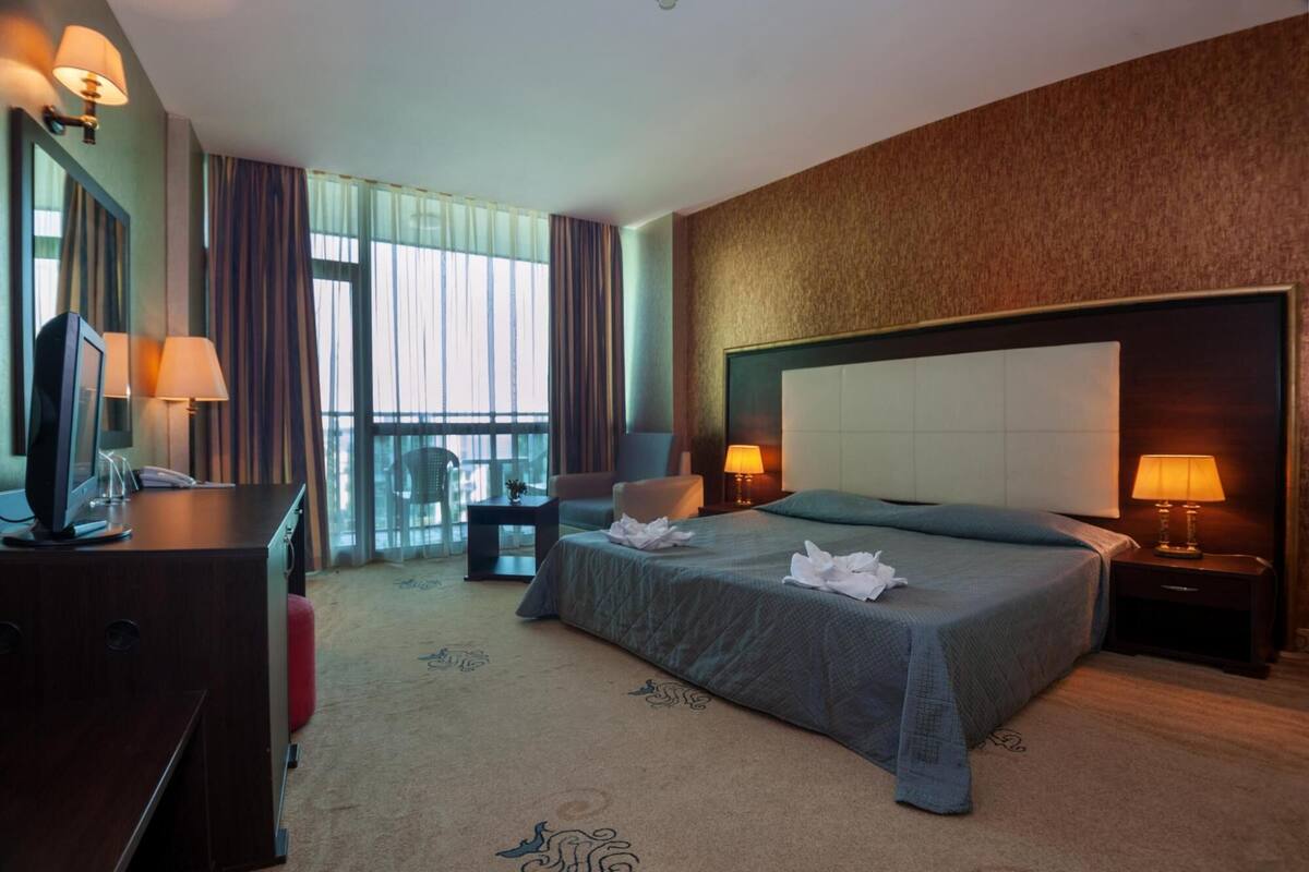 A hotel room with a large bed, a desk with a computer, a chair, and a view of the outdoors.