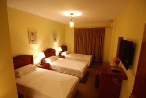 A hotel room with two beds, a desk with a TV, and a window with curtains.