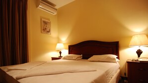 A hotel room with a large bed, two bedside lamps, a wooden headboard, a nightstand, and an air conditioning unit on the wall. - Al Rashid Hotel (Wadi Musa)