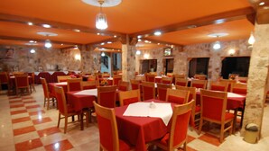 A restaurant with red tablecloths and wooden chairs, stone walls, and a checkered floor. - Al Rashid Hotel (Wadi Musa)