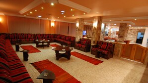 A hotel lobby with a large curved sofa, multiple armchairs, a coffee table, and a bar area. - Al Rashid Hotel (Wadi Musa)
