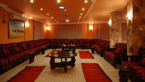 A large, well-lit room with a central seating area featuring multiple sofas and tables, surrounded by stone walls and red carpets. - Al Rashid Hotel (Wadi Musa)