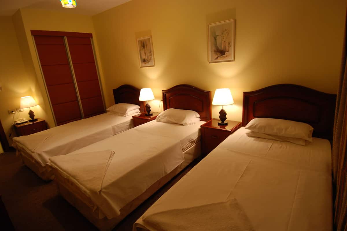 A hotel room with two single beds, each with a nightstand and lamp, a red wardrobe, and two wall-mounted paintings.