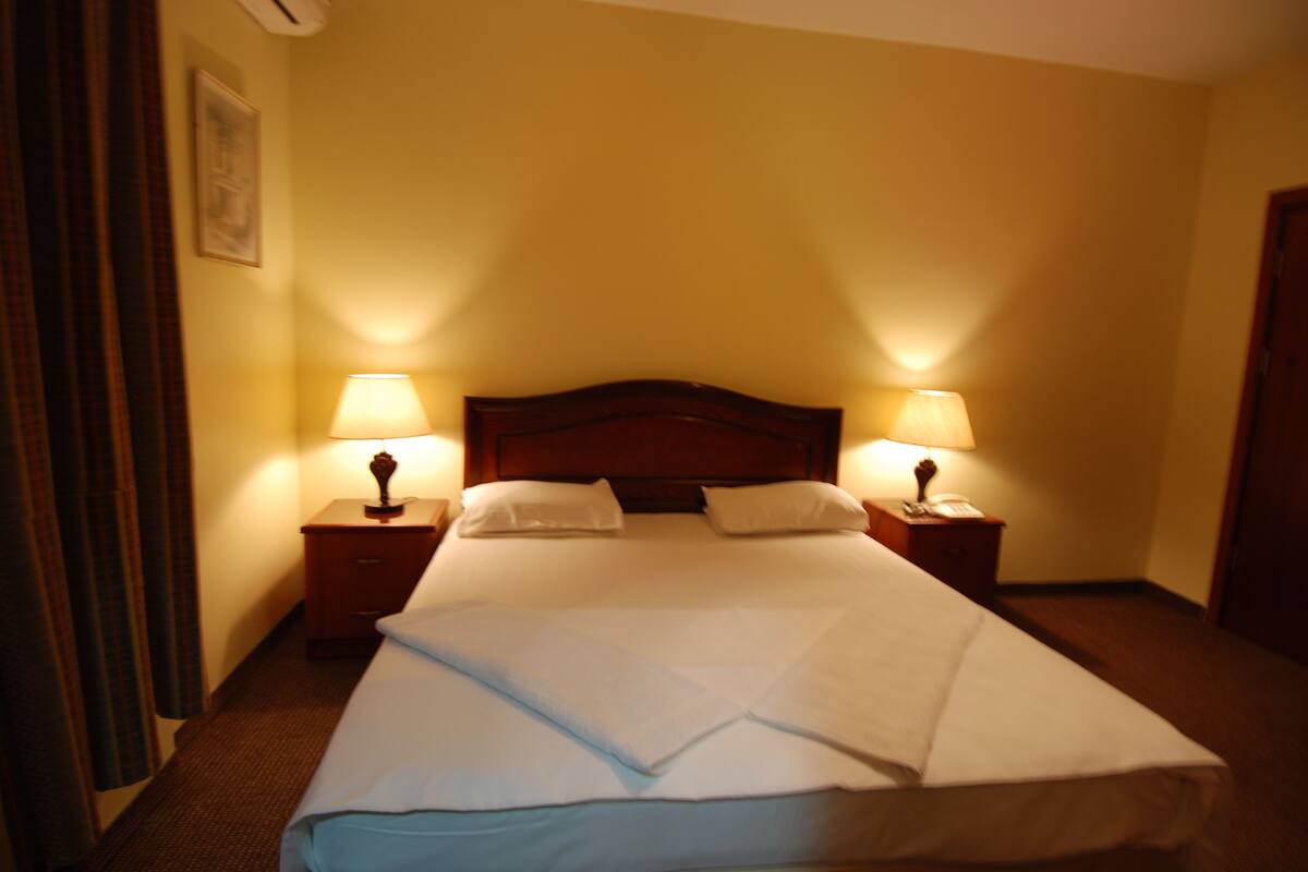 A hotel room with a large bed, two bedside tables with lamps, and a headboard.