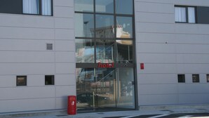 Fachada moderna de un hotel con una entrada de vidrio grande, un toldo rojo y un letrero que dice 'hotel'.