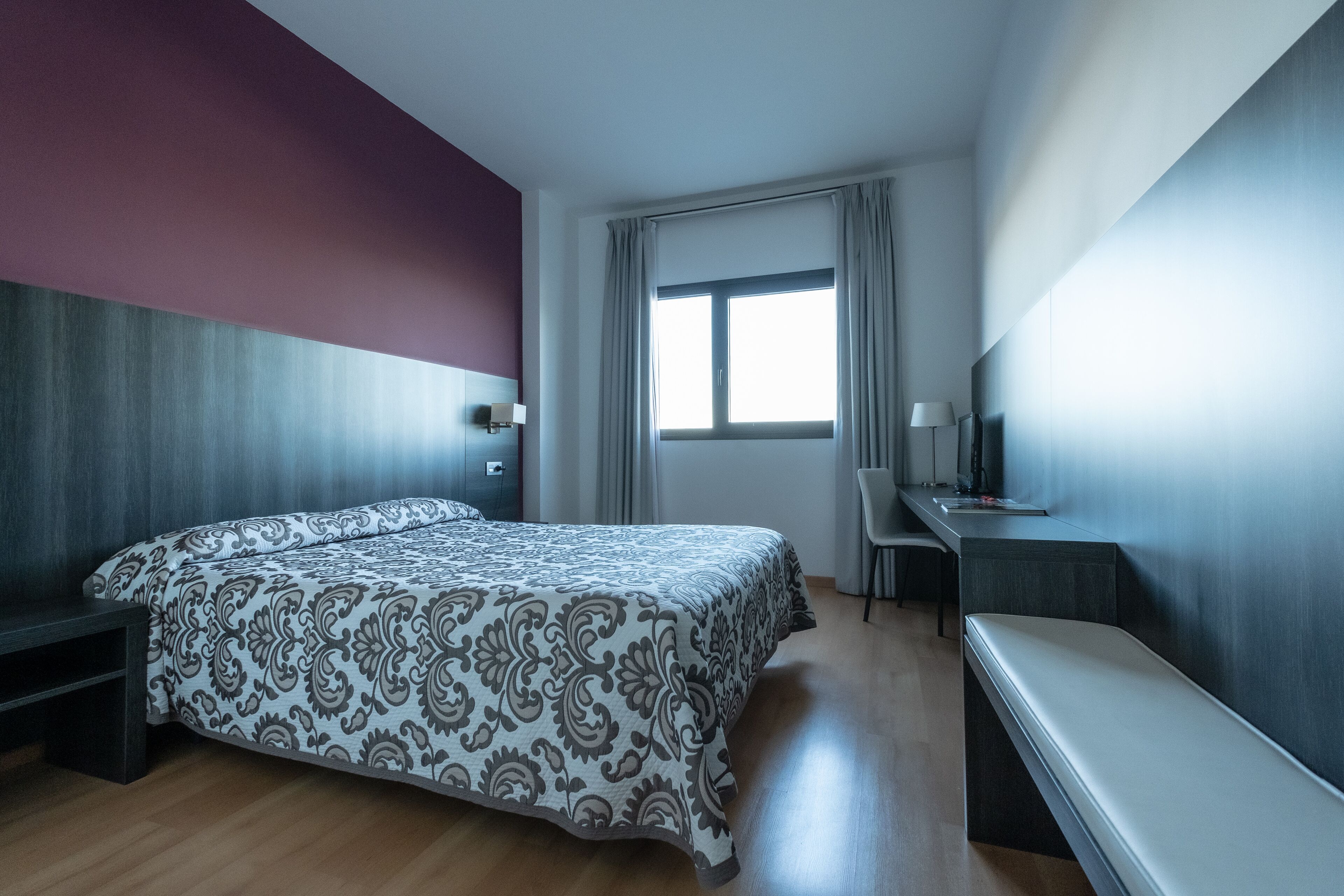 A modern hotel room with a large bed, a desk, and a chair.