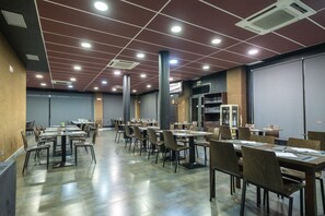 Un amplio comedor con varias mesas y sillas, suelo de baldosas e iluminación empotrada en un techo moderno.