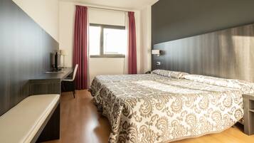 Una habitación de hotel moderna con una cama grande, un escritorio con una silla y una ventana con cortinas.