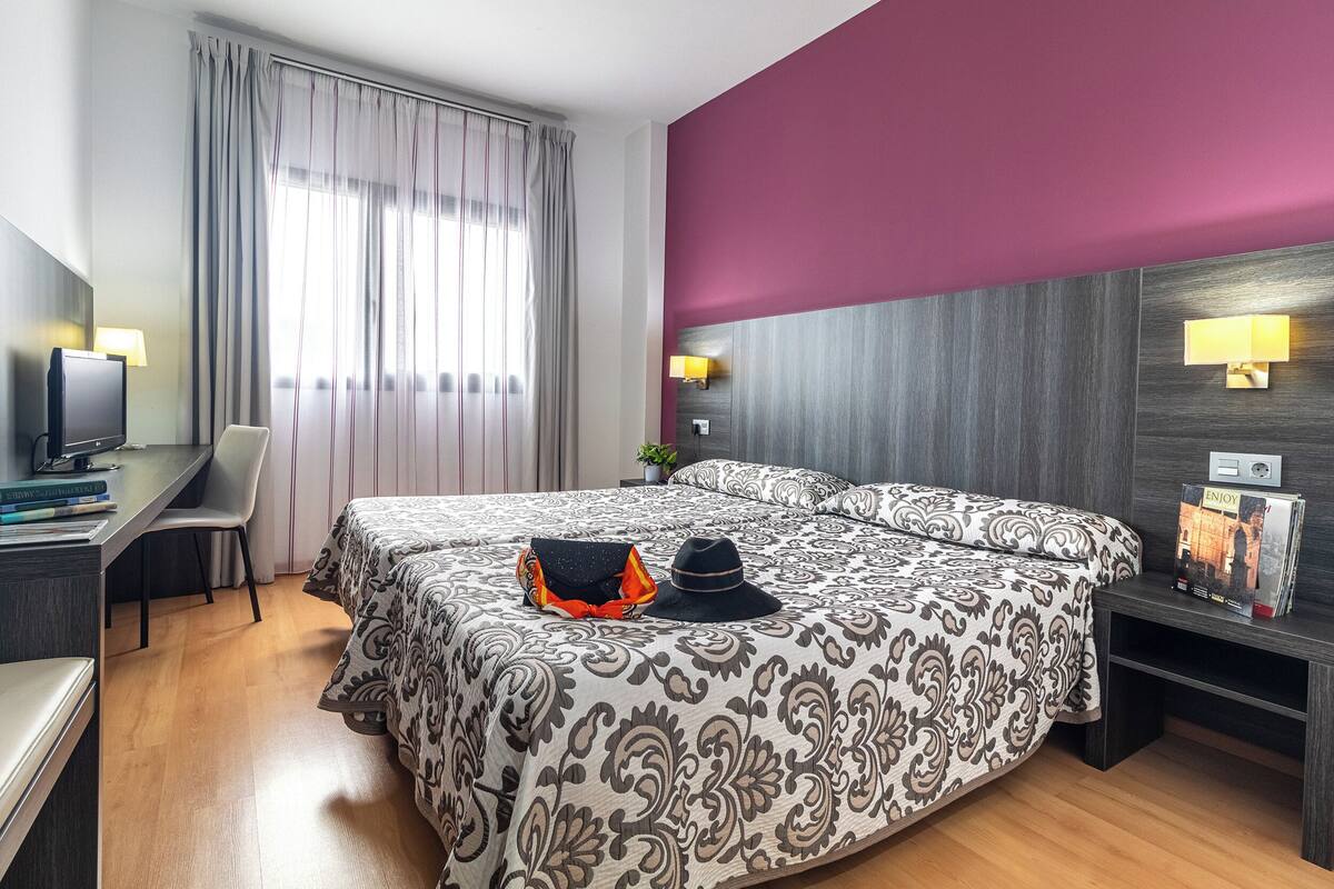 Una habitación de hotel con una cama grande, un escritorio con una computadora y un televisor.