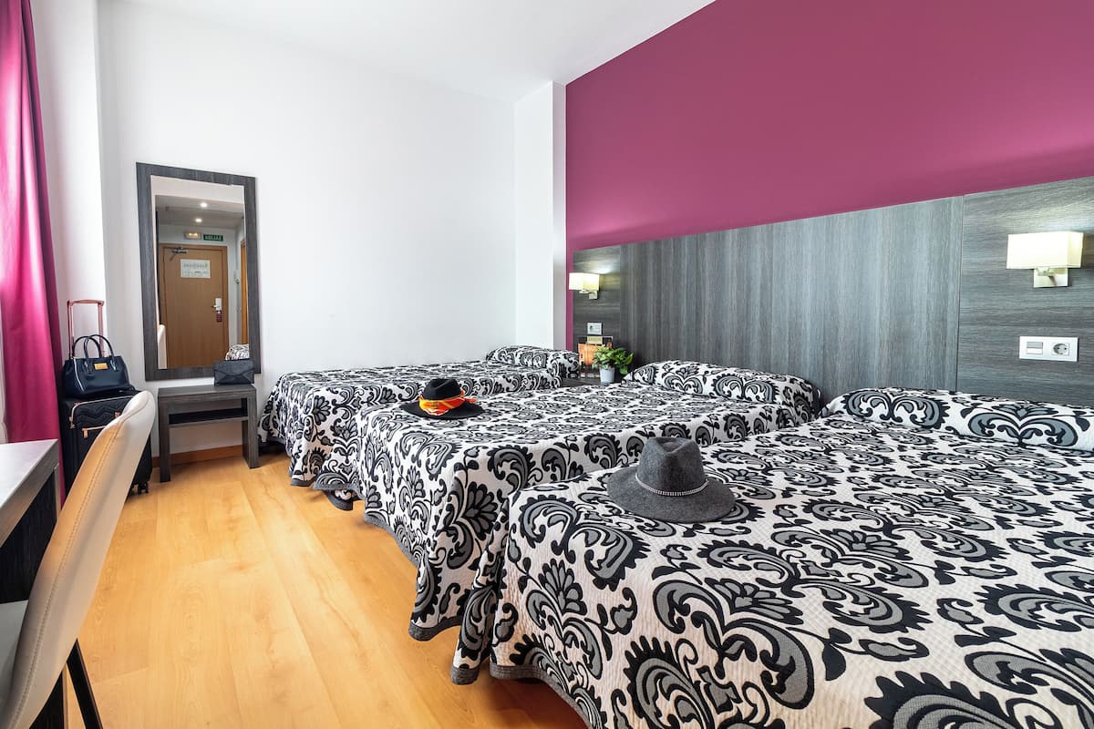 Habitación de hotel con dos camas, un escritorio, un espejo y una puerta.