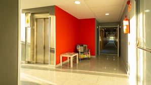 Pasillo de hotel con pared roja, extintor y una silla infantil.