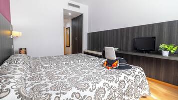A bedroom with a patterned bedspread, a television on a wooden shelf, and a potted plant.