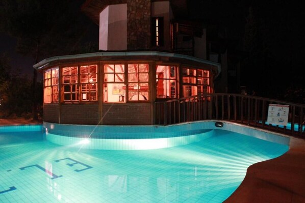 A swimming pool with a glass-enclosed structure, a tiled deck, and a stone building in the background. - Elze Hotel (Fethiye)