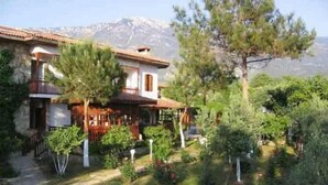 Un bâtiment à deux étages doté d’un balcon, entouré de verdure et avec une montagne en arrière-plan.