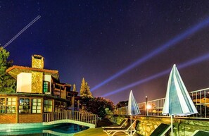 A nighttime view of a resort with a swimming pool, lounge chairs, and a stone building with a chimney. - Elze Hotel (Fethiye)