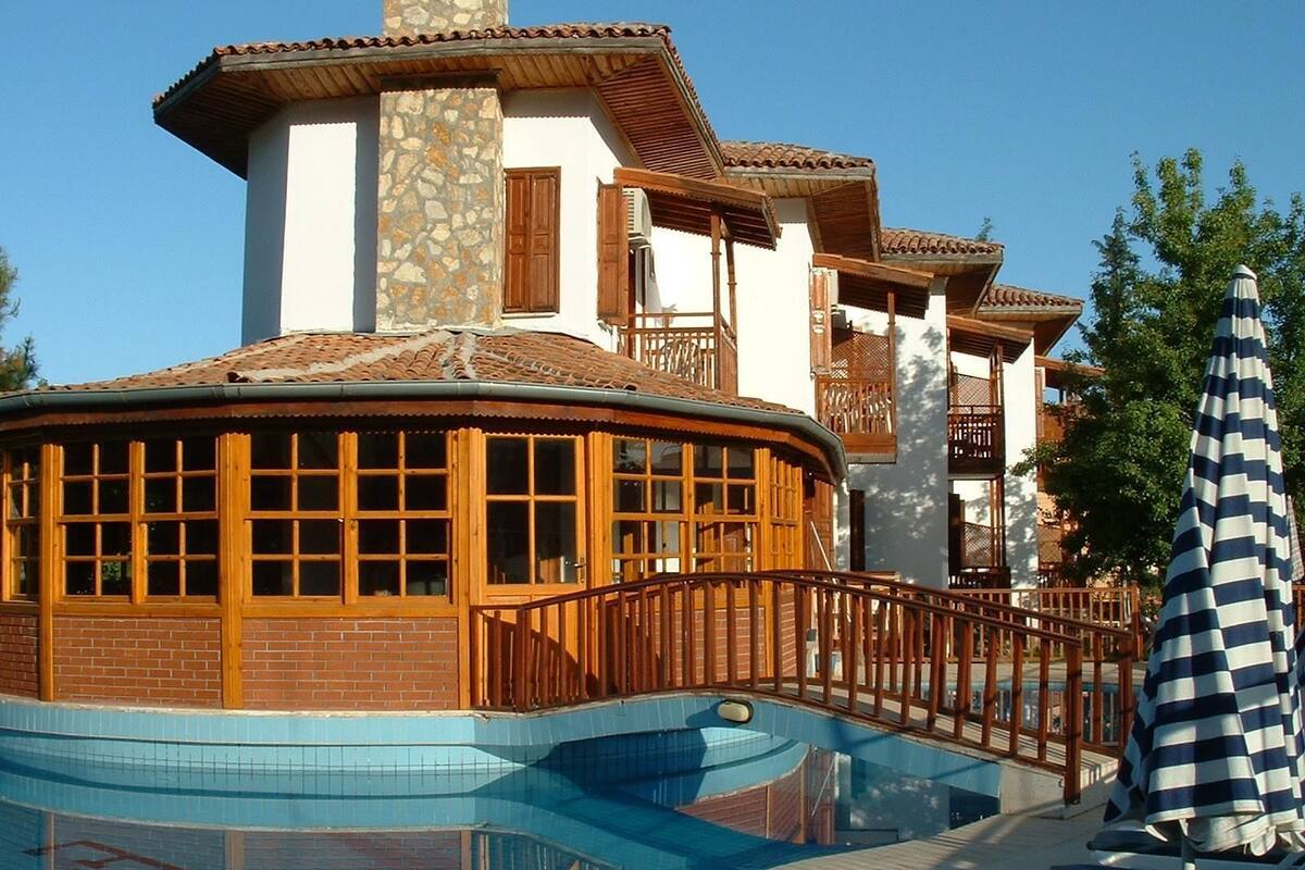 A resort with a swimming pool, wooden deck, and a covered area with a view of the pool.