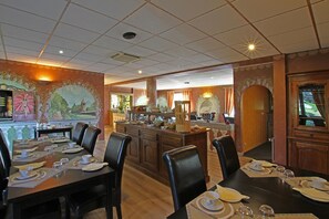 Un comedor con una mesa larga dispuesta para una comida, una zona de bar con mostrador y taburetes, y un mural en la pared que representa un paisaje.