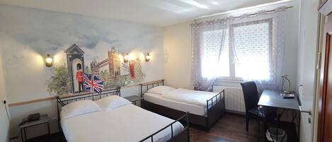 Habitación de hotel con dos camas individuales, un escritorio, una silla, un radiador y un mural con un paisaje urbano.
