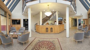 A spacious lobby with a central bar area, seating arrangements, and a staircase leading to upper floors. - Hôtel Champ Alsace Aerodrome (Haguenau)
