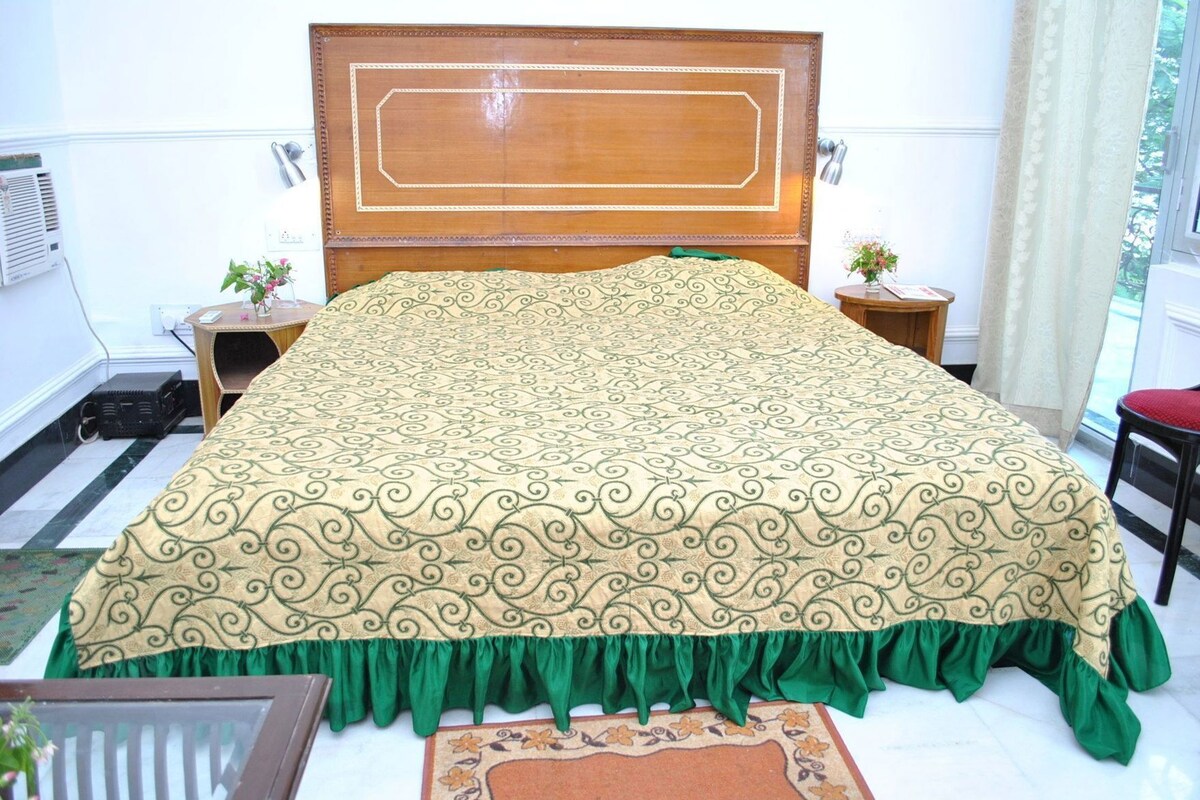 Un lit avec une couvre-lit à motifs, une tête de lit en bois, des tables de chevet avec des lampes et une fenêtre avec des rideaux.