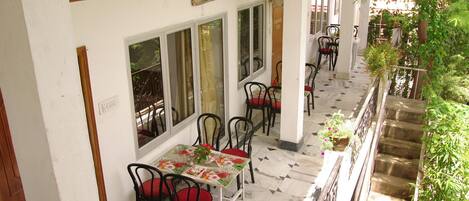 A corridor with tables and chairs, a tiled floor, and a staircase with greenery.