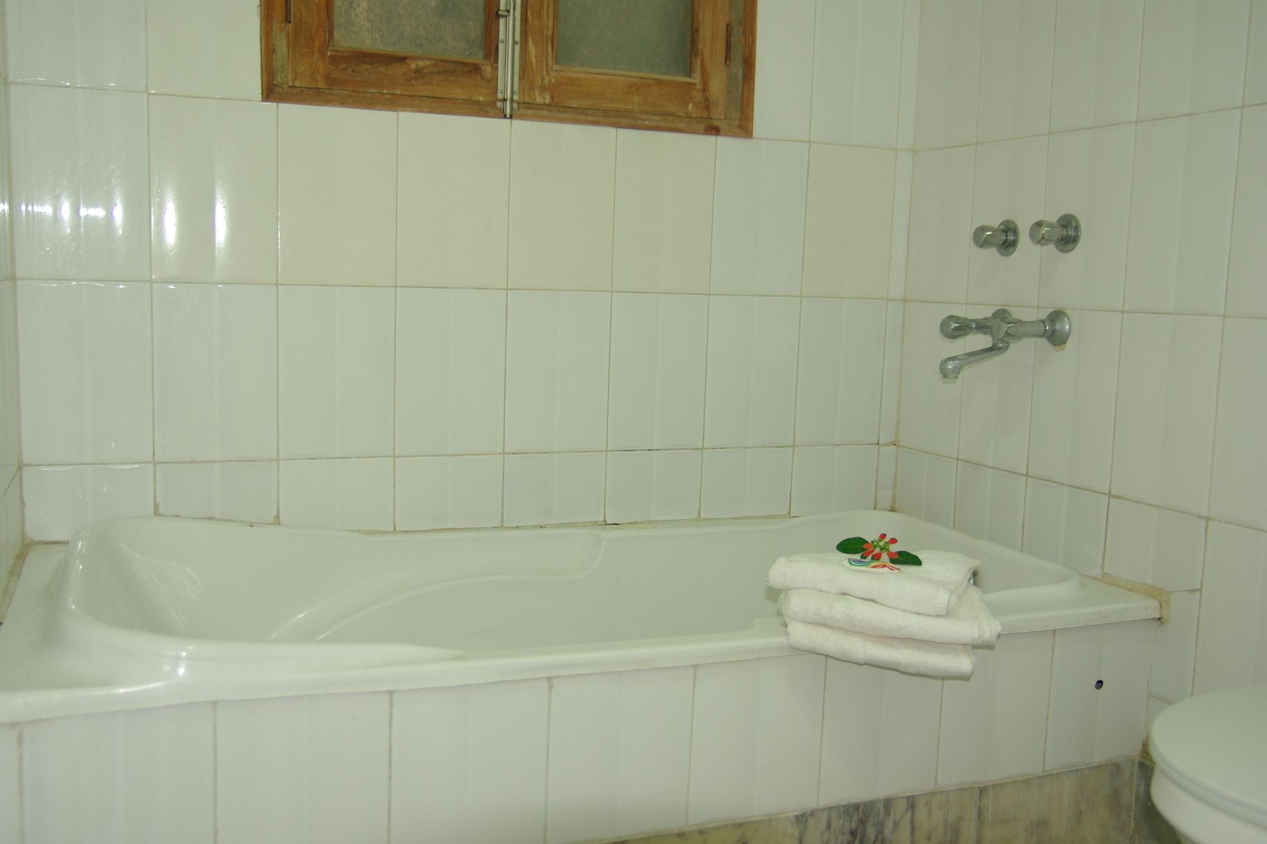 A bathroom with a white bathtub, a wooden-framed window, and a toilet.