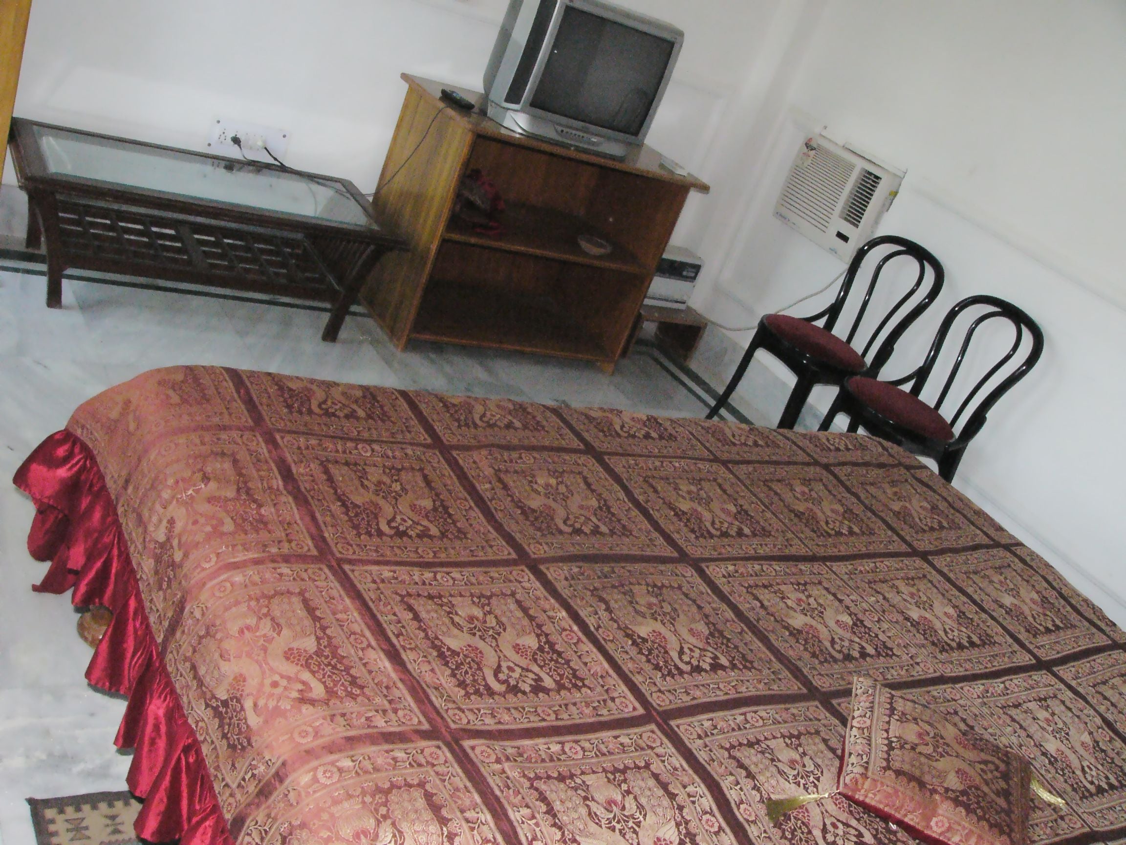 A room with a bed, a television on a wooden stand, and a chair.