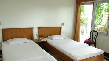 Une chambre avec deux lits simples, une table de chevet avec une bouteille d’eau et un vase de fleurs, une chaise et une fenêtre donnant sur un paysage verdoyant.