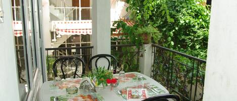 A table set for two on a balcony with a view of a building and greenery.