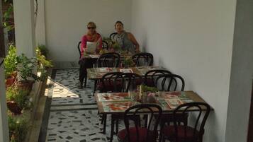 A patio area with tables and chairs, potted plants, and a tiled floor.