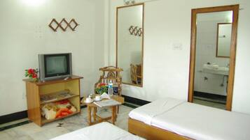 A hotel room with two beds, a television on a wooden stand, a chair, a small table with a newspaper, and a bathroom visible through a mirror.