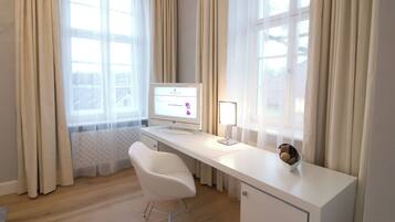 Un escritorio moderno blanco con una computadora, una silla y una lámpara en una habitación con ventanas grandes y cortinas.