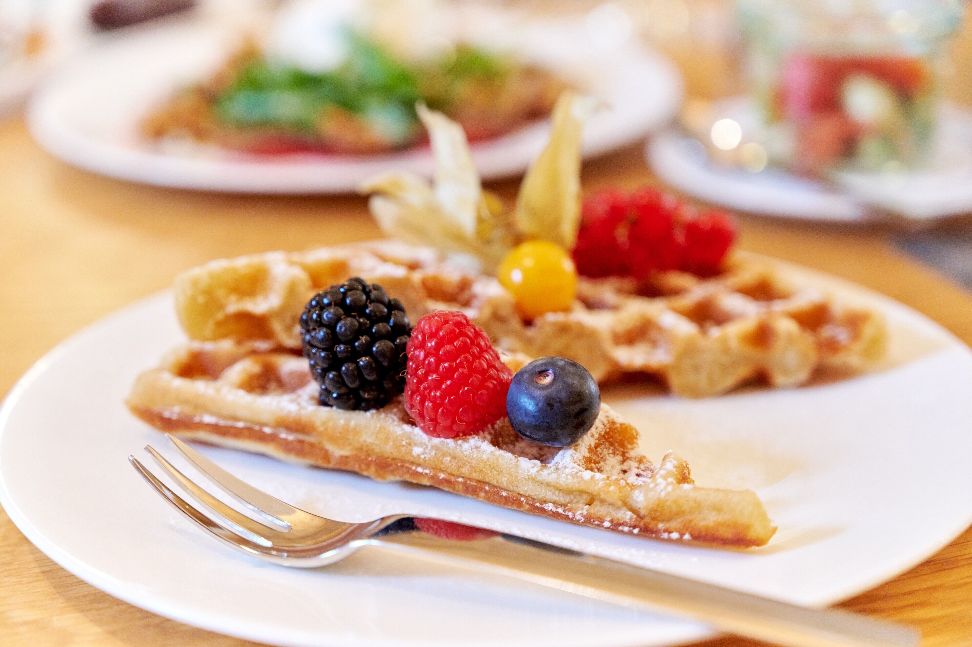 A close-up of a slice of Belgian waffle with fresh berries and powdered sugar on a white plate.