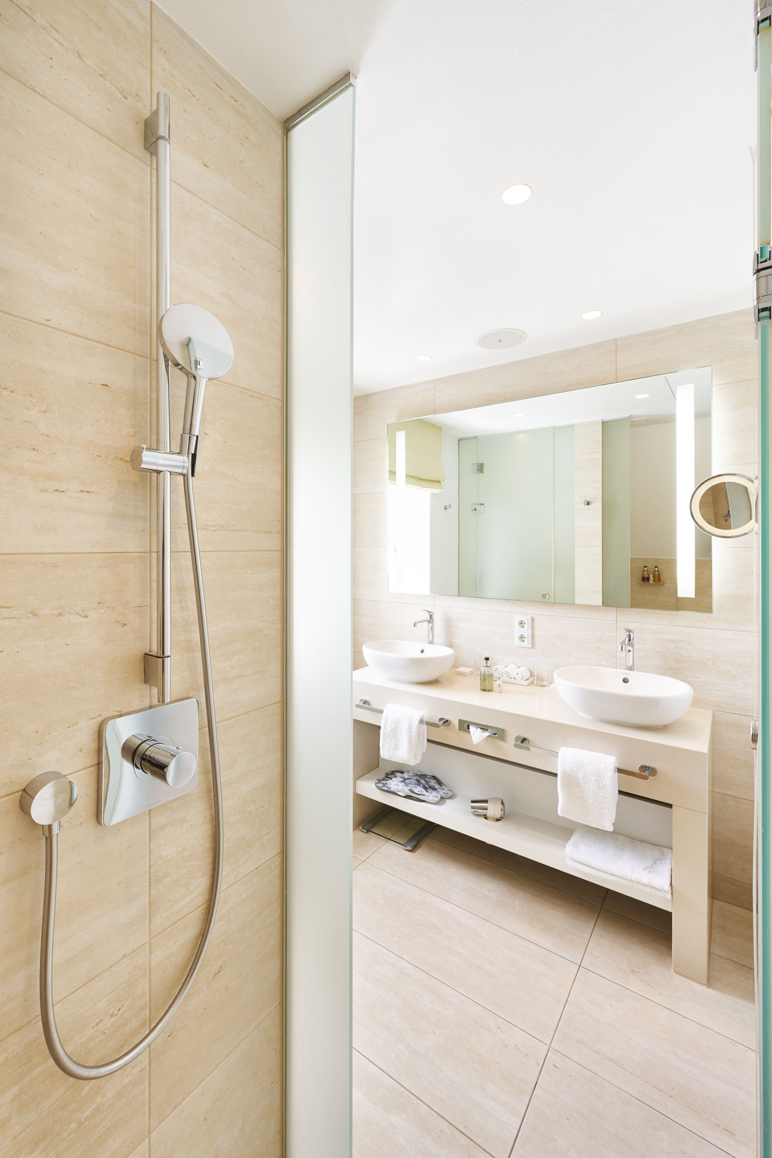 Een moderne badkamer met een inloopdouche, twee wastafels, een grote spiegel en een meubel met daaraan een handdoekhouder.