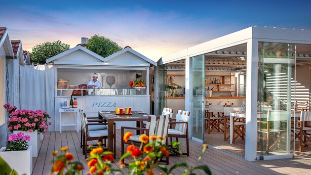 An outdoor dining area with a pizza bar, wooden deck, and glass-enclosed seating. - Hotel Principe Forte dei Marmi (Forte dei Marmi)