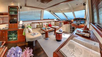 Un intérieur de yacht luxueux, avec un coin salon confortable, un meuble en bois doté de portes en verre et une vue sur la mer grâce à de grandes fenêtres.
