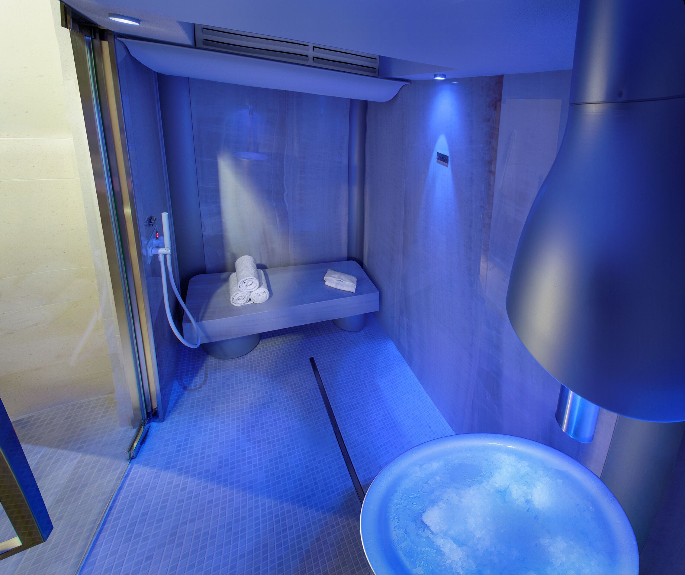 A modern bathroom with a built-in shower, a bench with towels, and a large basin.