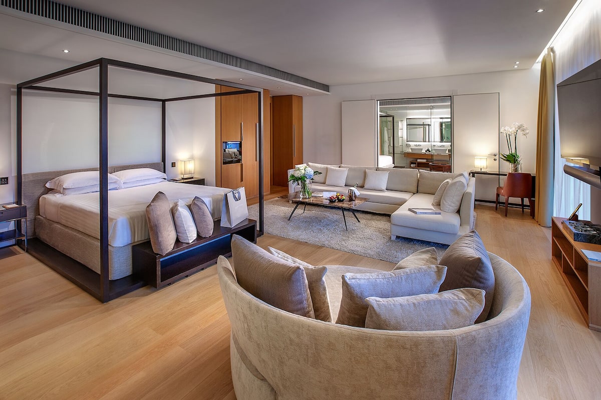 A modern hotel room with a four-poster bed, a sofa, a coffee table, and a chair.