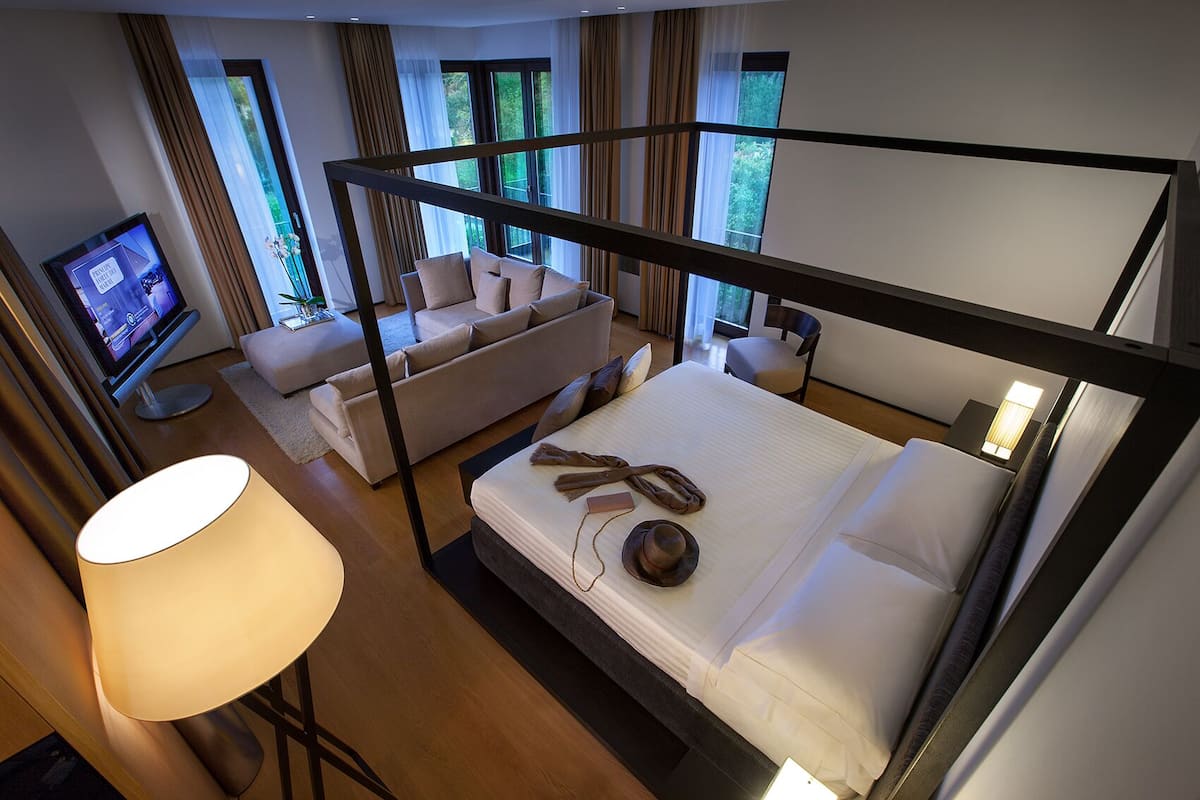 A modern hotel room with a bunk bed, a sofa, a TV, and a lamp.