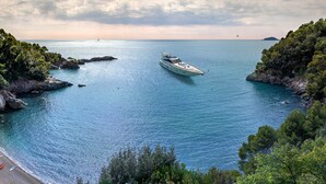 A yacht anchored near a rocky coastline with a beach and dense greenery. - Hotel Principe Forte dei Marmi (Forte dei Marmi)