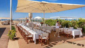 An outdoor dining area with tables and chairs, a waiter, and a view of the beach and ocean. - Hotel Principe Forte dei Marmi (Forte dei Marmi)