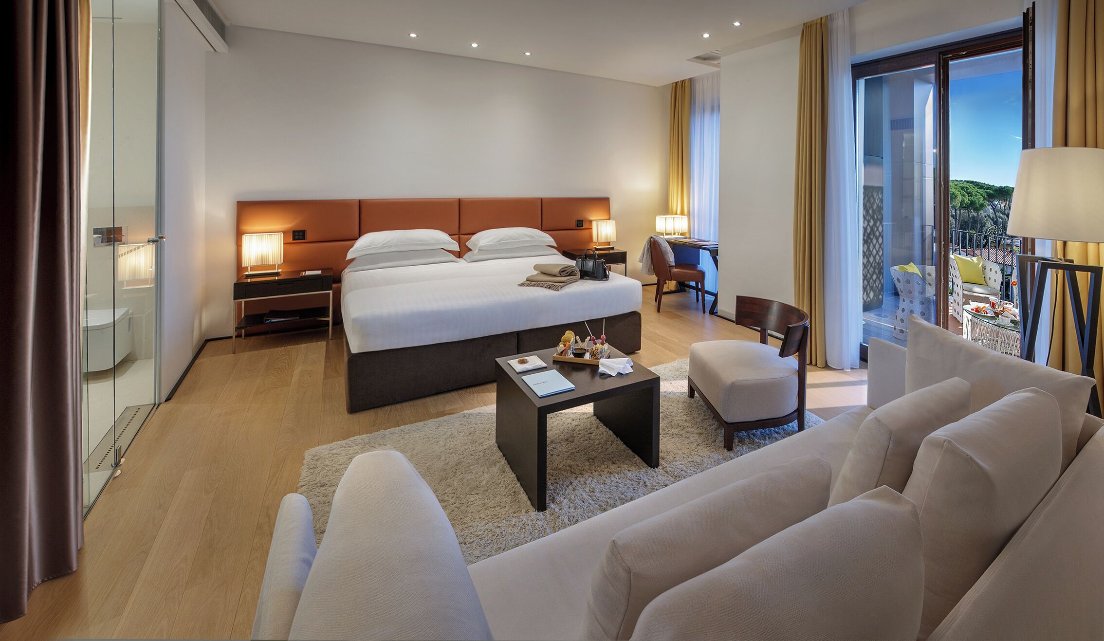 A modern hotel room with a large bed, bedside tables, a desk, and a view of the outdoors.