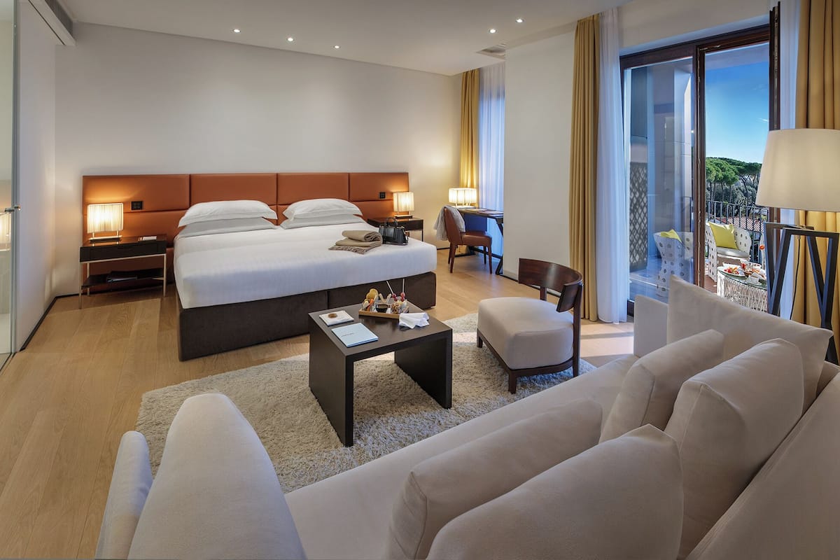 A modern hotel room with a large bed, bedside tables, a desk, and a view of the outdoors.