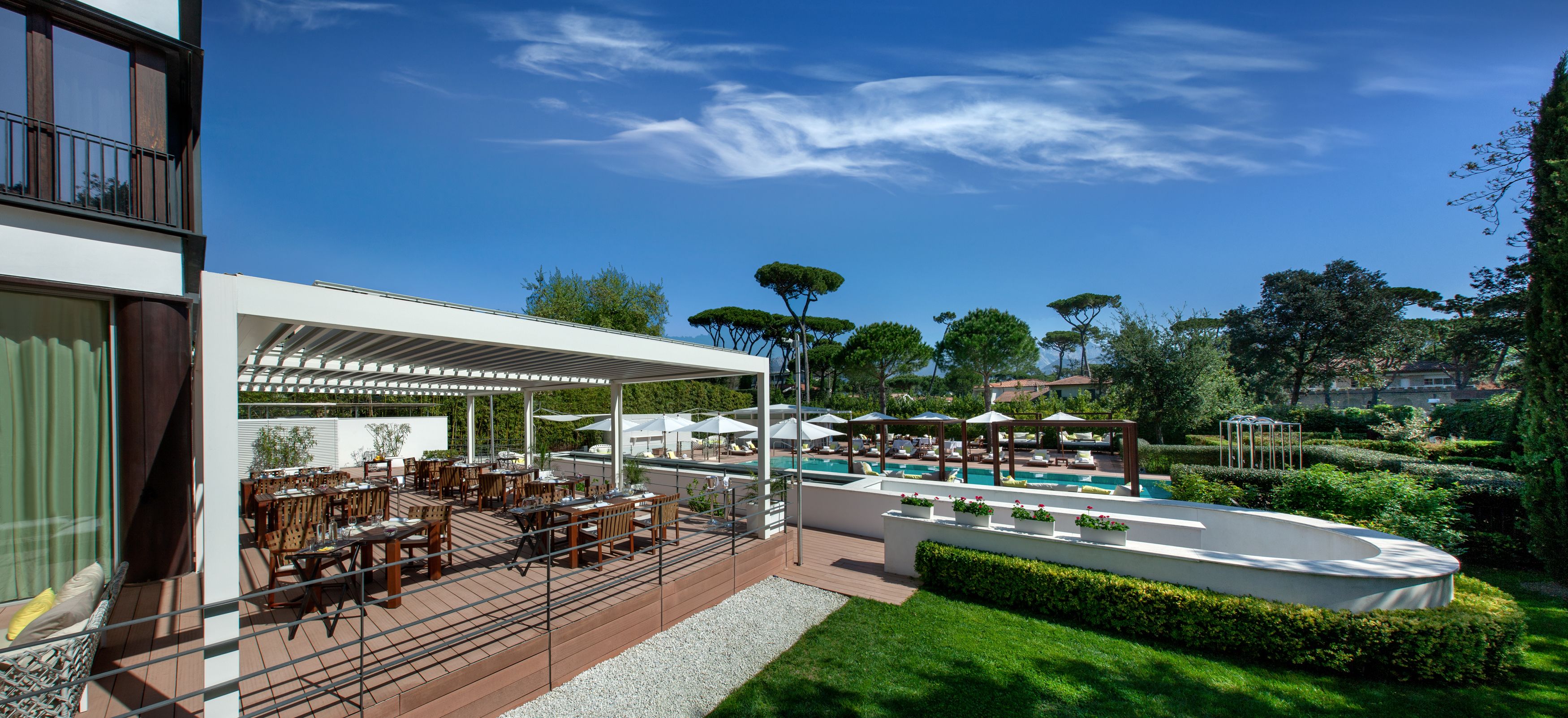 A modern outdoor dining area with tables and umbrellas, a pool, and well-maintained landscaping.